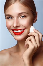 Beautiful girl with red lips and classic makeup with foundation sponge in hand. Beauty face. Photo taken in the studio