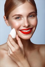 Beautiful girl with red lips and classic makeup with foundation sponge in hand. Beauty face. Photo taken in the studio