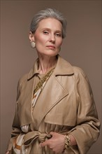Portrait of a beautiful elderly woman in a beige raincoat with classic makeup and gray hair