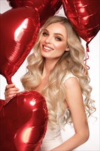 Sexy woman in white dress and balloons with hearts posing in the studio on Valentine's Day