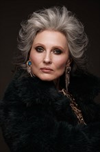 Portrait of a beautiful elderly woman in a leopard blouse and fur coat with classic makeup and gray hair