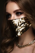 Portrait of a beautiful woman in a gold mask with sequins and classic makeup. Mask mode during the covid pandemic