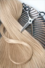 A strand of blond hair with scissors on a white background. Close-up