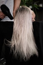 Young woman in a hairdressing salon dyes her hair blond and dries hair