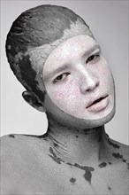 Young man with art creative make-up with mud on his face. Cosmetic mask. Beauty face. Picture taken in the studio on a black background