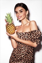 Beautiful sexy woman with pineapple in hands in a leopard dress and earrings
