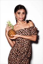 Beautiful sexy woman with pineapple in hands in a leopard dress and earrings