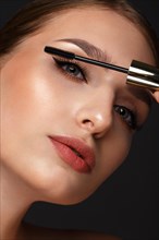 Beautiful girl with sexy lips and classic makeup with cosmetic mascara brush in hand. Beauty face. Photo taken in the studio