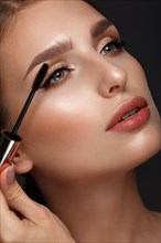 Beautiful girl with sexy lips and classic makeup with cosmetic mascara brush in hand. Beauty face. Photo taken in the studio