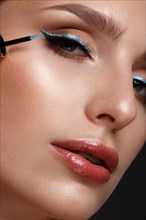 Beautiful girl with sexy lips and classic makeup with cosmetic blue eyeliner in hand. Beauty face. Photo taken in the studio