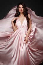 Beautiful brunette woman with curls and classic make-up in a flying light pink dress. Beauty face. Photo taken in studio