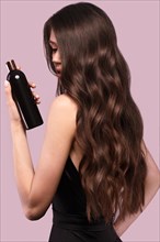 Beautiful brunette woman with curls and classic make-up in a black dress with a bottle of shampoo in hands. Beauty face. Photo taken in studio