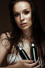 Beautiful girl with a bright make-up and wet hair and skin with bottle of cosmetic products in the hands. Beauty face. Picture taken in the studio on a black background