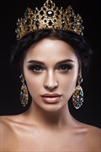 Beautiful brunette girl with a golden crown and earrings and professional evening make-up. Beauty face. Picture taken in the studio