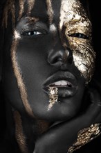 Fashion portrait of a dark-skinned girl with gold make-up.Beauty face. Picture taken in the studio on a black background