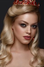 Beautiful blond girl with a golden crown and earrings and professional evening make-up. Beauty face. Picture taken in the studio