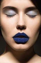 Portrait of beautiful girl with unusual blue lips and eyes closed. Picture taken in the studio on a gray background