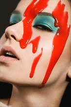 Portrait of a beautiful Girl with red paint on her face. Photo shot in the Studio on a black background