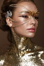 Beautiful girl in a golden mask and bright evening make-up. Beauty face. Photo taken in studio