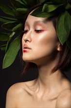 Beautiful Asian girl with a bright make-up art in green leaves. Beauty face. Creative image. Picture taken in the studio