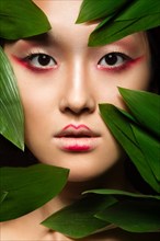 Beautiful Asian girl with a bright make-up art in green leaves. Beauty face. Creative image. Picture taken in the studio
