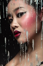 Beautiful Asian girl with bright make-up behind glass with drops of wax. Beauty face. Picture taken in the studio on a black background