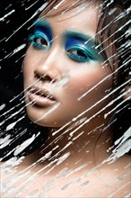 Beautiful Asian girl with bright blue make-up behind glass with drops of wax. Beauty face. Picture taken in the studio on a black background