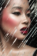Beautiful Asian girl with bright make-up behind glass with drops of wax. Beauty face. Picture taken in the studio on a black background