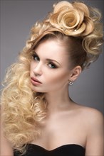 Beautiful blonde girl in evening dress with an unusual hairstyle in the form of roses and bright makeup. Beauty face. Picture taken in the studio on a gray background