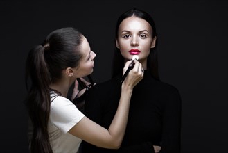 Two beautiful girls on a photo shoot to apply makeup to the face. Beauty fashion model. Photos shot in studio
