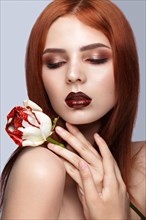Beautiful red-haired girl with a classic make-up and rose in her hands. Beauty face. Photo taken in studio