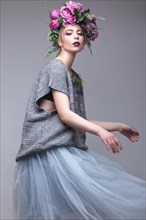 Beautiful girl with flowers on her head in fashion clothes posing against the background in the studio. Beauty Style