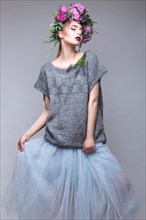 Beautiful girl with flowers on her head in fashion clothes posing against the background in the studio. Beauty Style