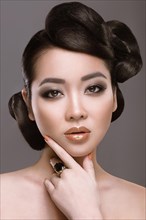 Beautiful girl with oriental type evening hair and makeup. Portrait shot in the studio on a gray background