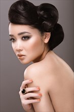 Beautiful girl with oriental type evening hair and makeup. Portrait shot in the studio on a gray background