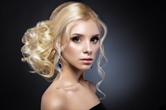 Beautiful blond girl in a black dress with evening haircut in the form of waves and bright makeup. Beauty face. Picture taken in the studio