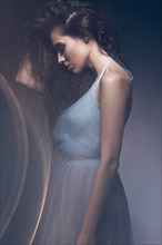 Beautiful girl in a light blue dress and long hair in a fashionable image. Beauty fashion style. Picture taken in the studio with mixed light