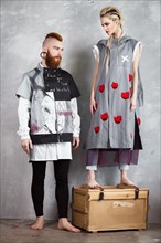 Creative unusual blond girl and red-haired man in designer clothes and braids on their heads posing in the studio