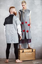 Creative unusual blond girl and red-haired man in designer clothes and braids on their heads posing in the studio