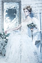 Beautiful girl in white dress in the image of the Snow Queen with a crown on her head. Picture taken in the studio with decorations