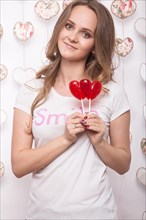 Valentines Day. Funny beautiful Woman holding candy in the form of heart. Beauty face. Picture taken in the studio with decorations