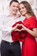 Beautiful young couple in love with a bouquet of flowers showing the form of heart hands. Valentine's Day. Picture taken in the studio
