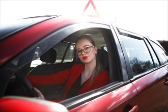 Young beautiful happy woman in red sitting at the wheel new training car