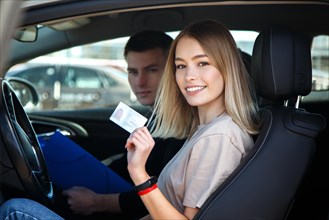 Joyful girl driving a training car with a drivers license card in her hands
