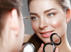Beautiful girl makes herself a make-up in the mirror. Beauty face. Photo taken in studio