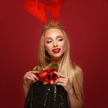 Beautiful blonde girl in a New Year's image with Christmas bells around her neck and deer horns on her head. Beauty face with festive makeup. Photo taken in the studio