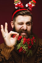 Funny bearded man in a New Year's image as Santa Claus with decorations on his beard. Feast of Christmas. Photos shot in the studio