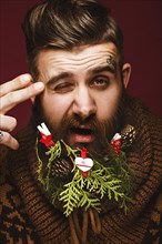 Funny bearded man in a New Year's image as Santa Claus with decorations on his beard. Feast of Christmas. Photos shot in the studio