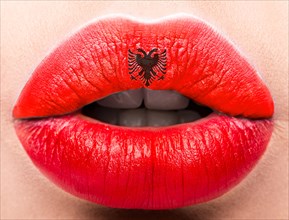 Female lips close up with a picture of the flag of Albania. Red and black emblem