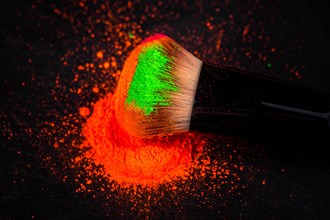 Cheek brush with neon cosmetic powder colorful pile and isolated on black background
